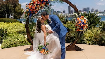 A couple kissing under a floral arch with a city skyline in the background.