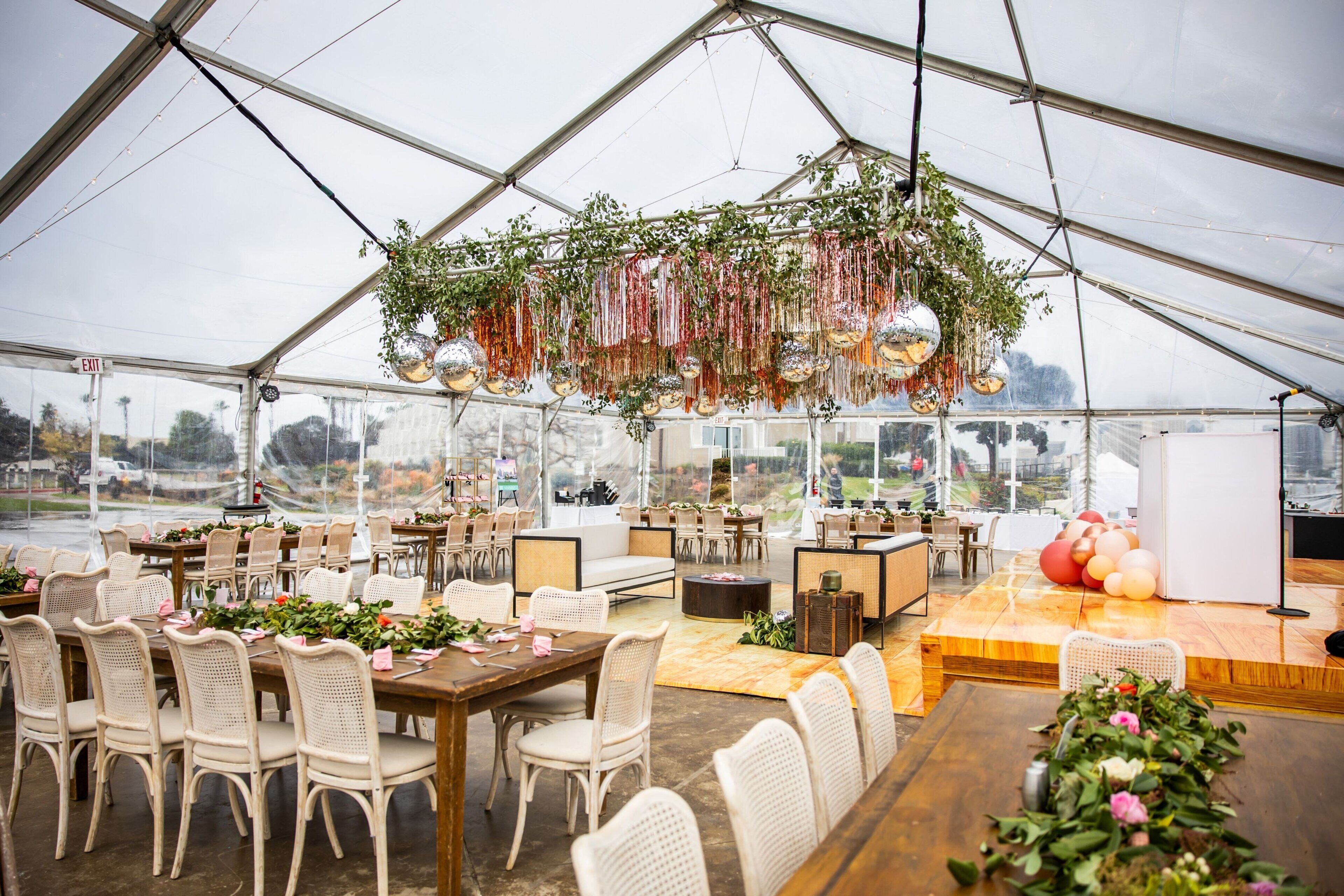 A tented event space with tables and chairs, hanging decorations, and a stage area.