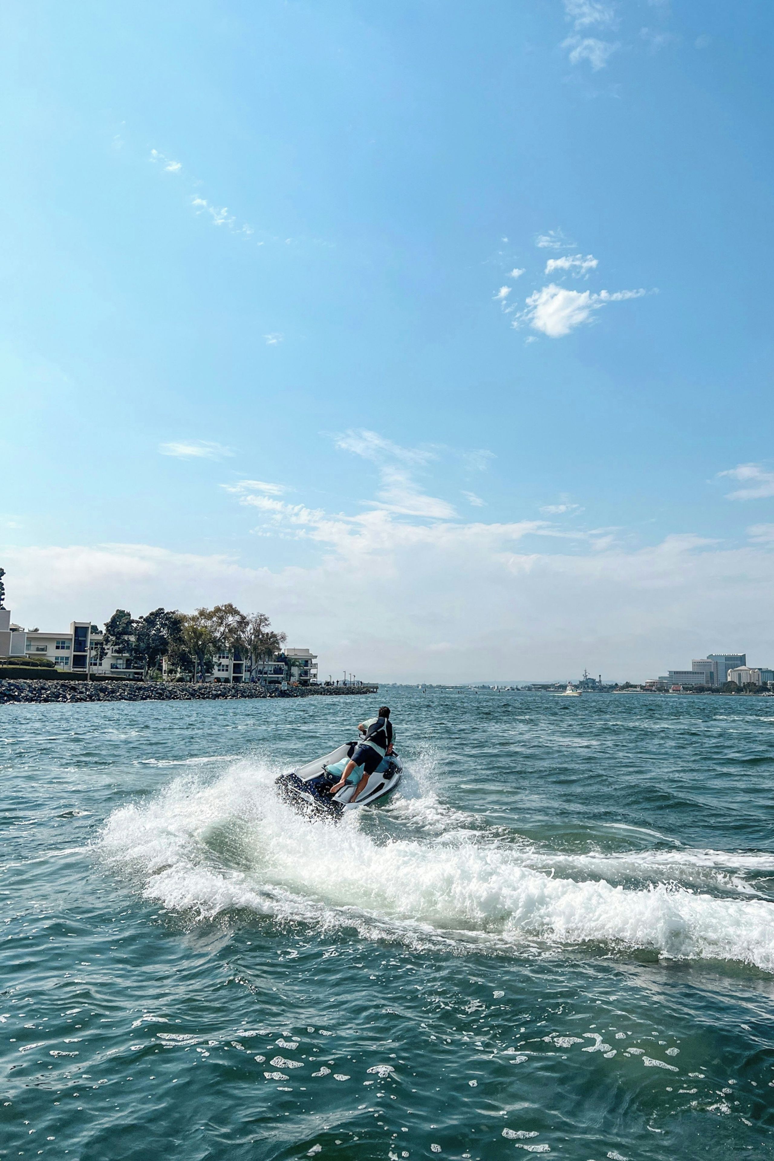 Une personne pratiquant le jet-ski sur une  étendue d’eau, avec des bâtiments en arrière-plan.