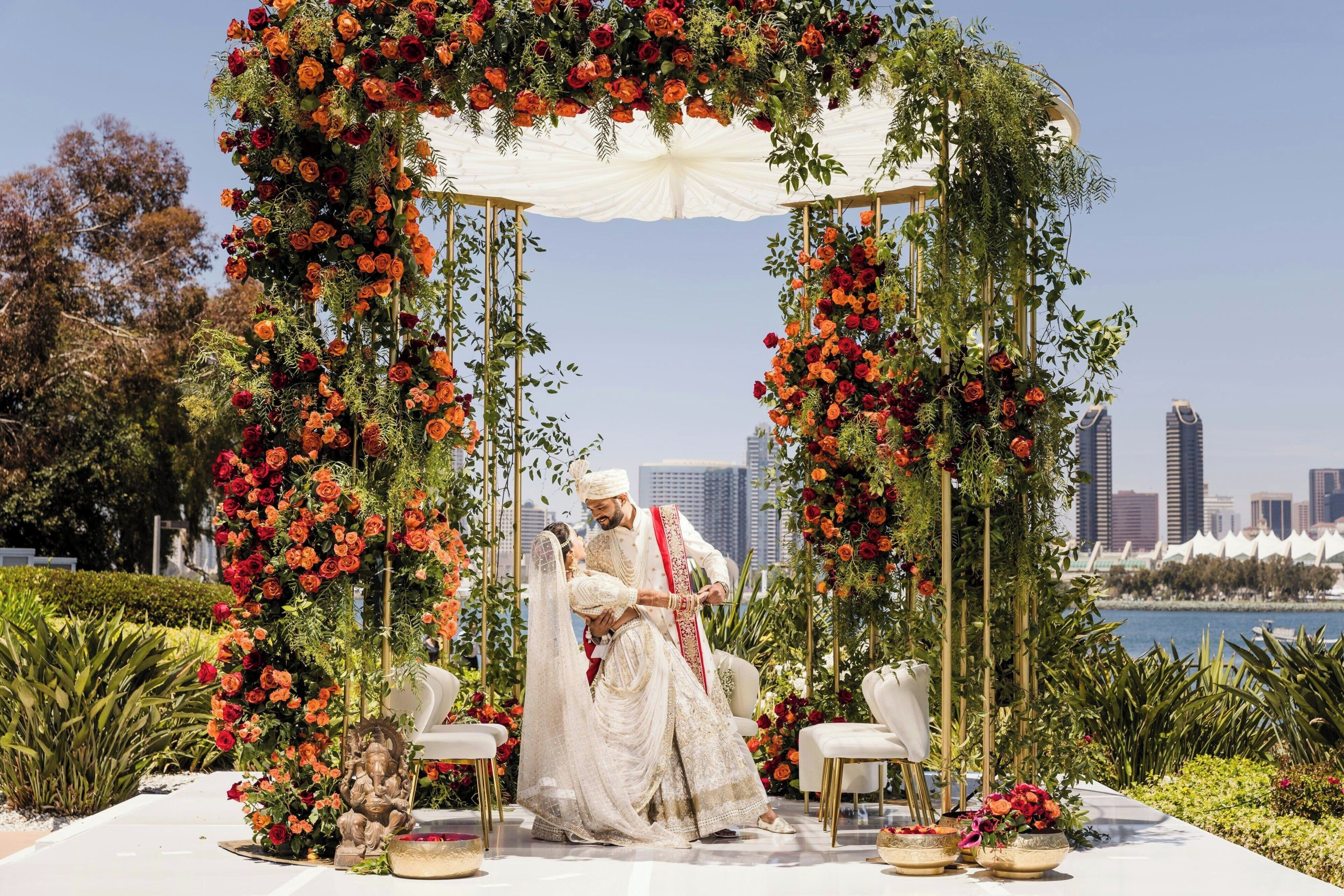 A couple seated under a floral arch with a city skyline in the background.