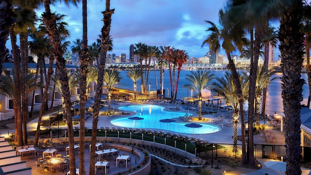 A resort pool area with palm trees, lounge chairs, and a city skyline in the background. - Coronado Island Marriott Resort & Spa (Coronado)