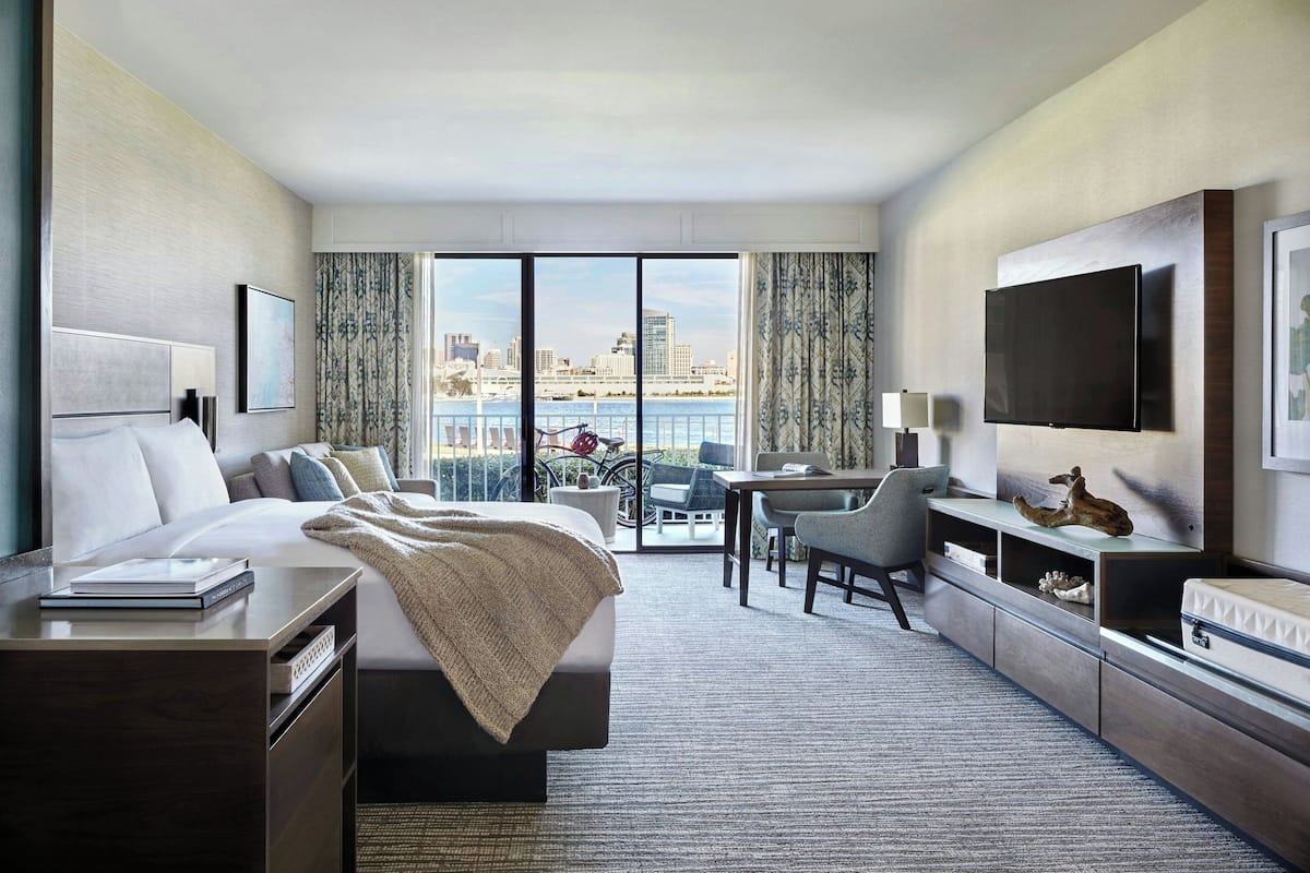 A modern hotel room with a large bed, a desk, a television, and a city view.