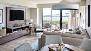 A modern living room with a large flat-screen TV, comfortable seating, a dining area, and a view of a bridge and water. - Coronado Island Marriott Resort & Spa (Coronado)