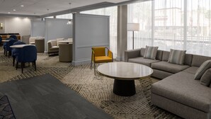 A modern hotel lobby with a seating area, a round coffee table, and large windows.