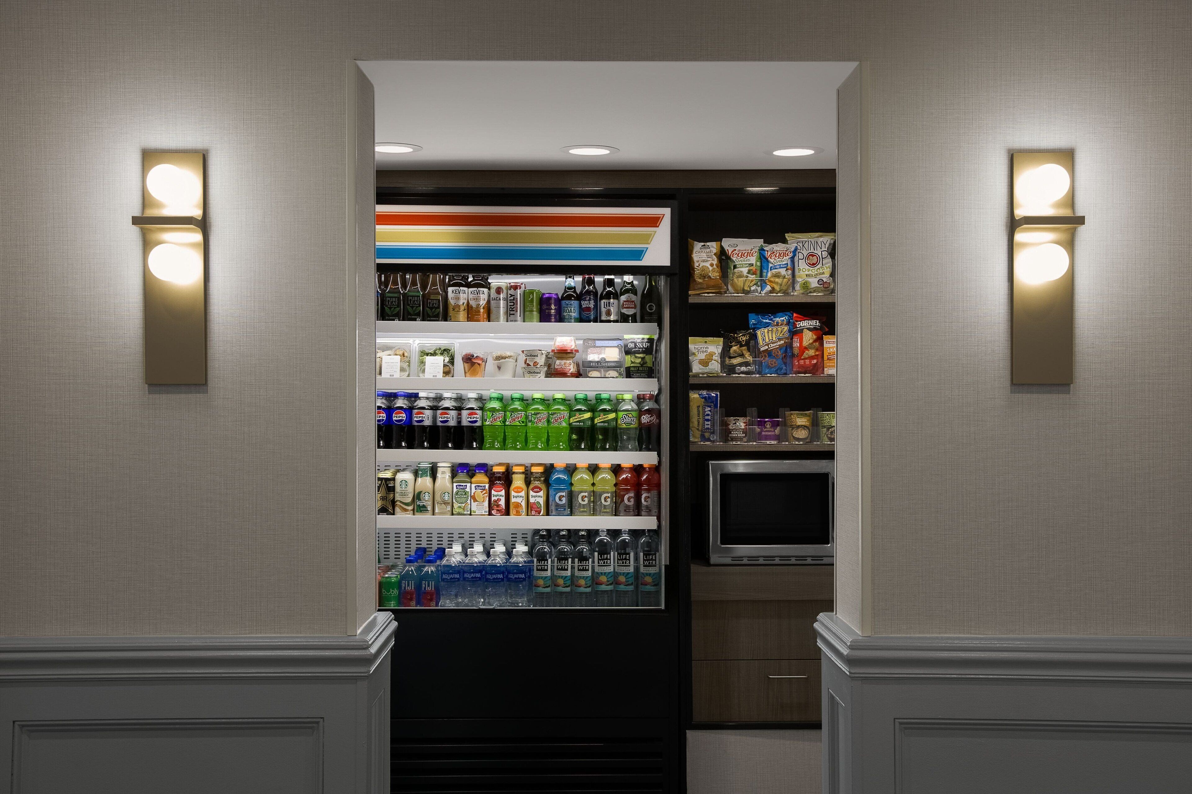 Un minibár de hotel con una variedad de bebidas y aperitivos, como refrescos, agua y bocadillos.
