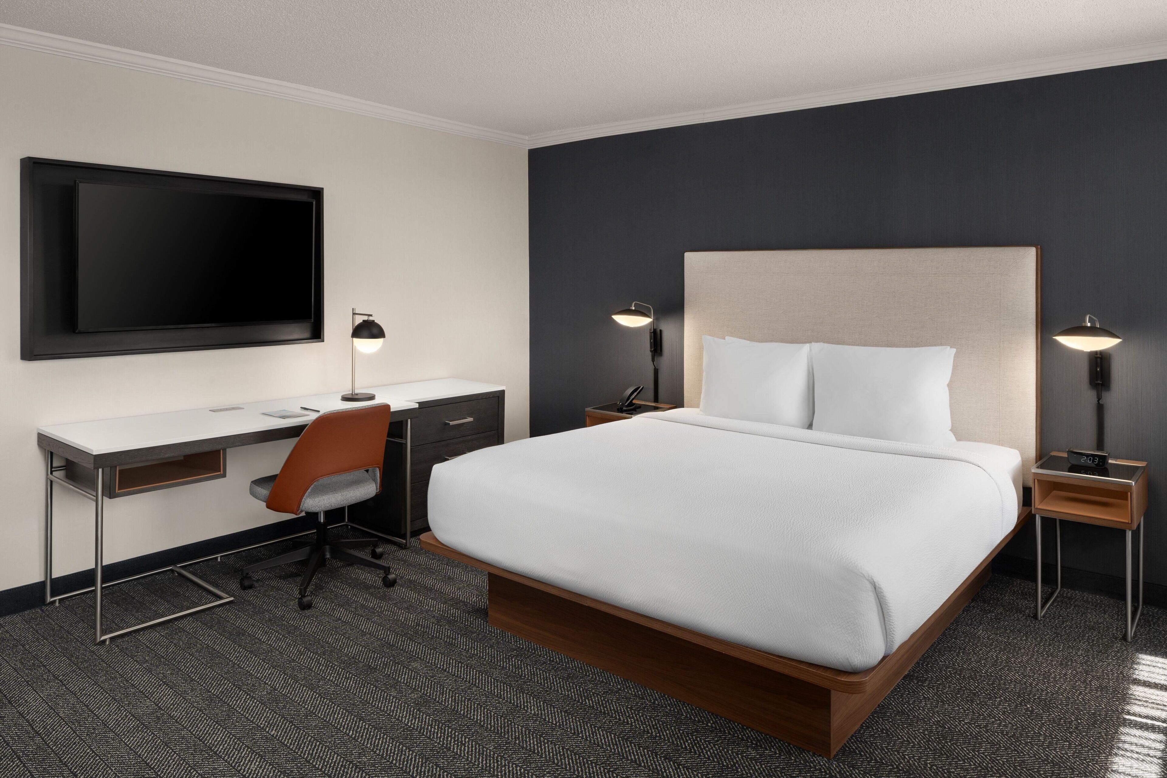 A modern hotel room with a large bed, a desk, and a flat-screen TV.