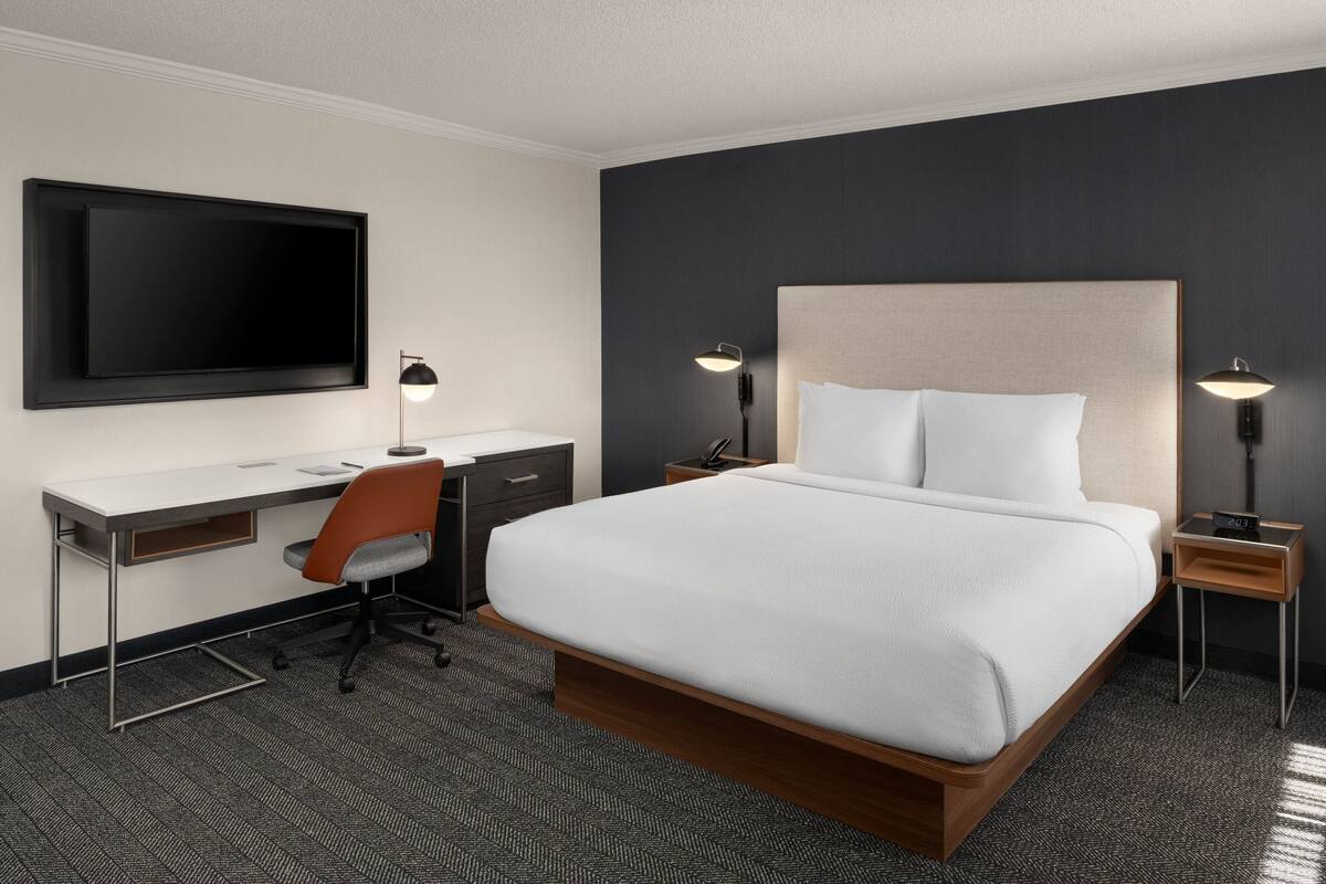 Una habitación de hotel moderna con una cama grande, un escritorio y un televisor de pantalla plana.