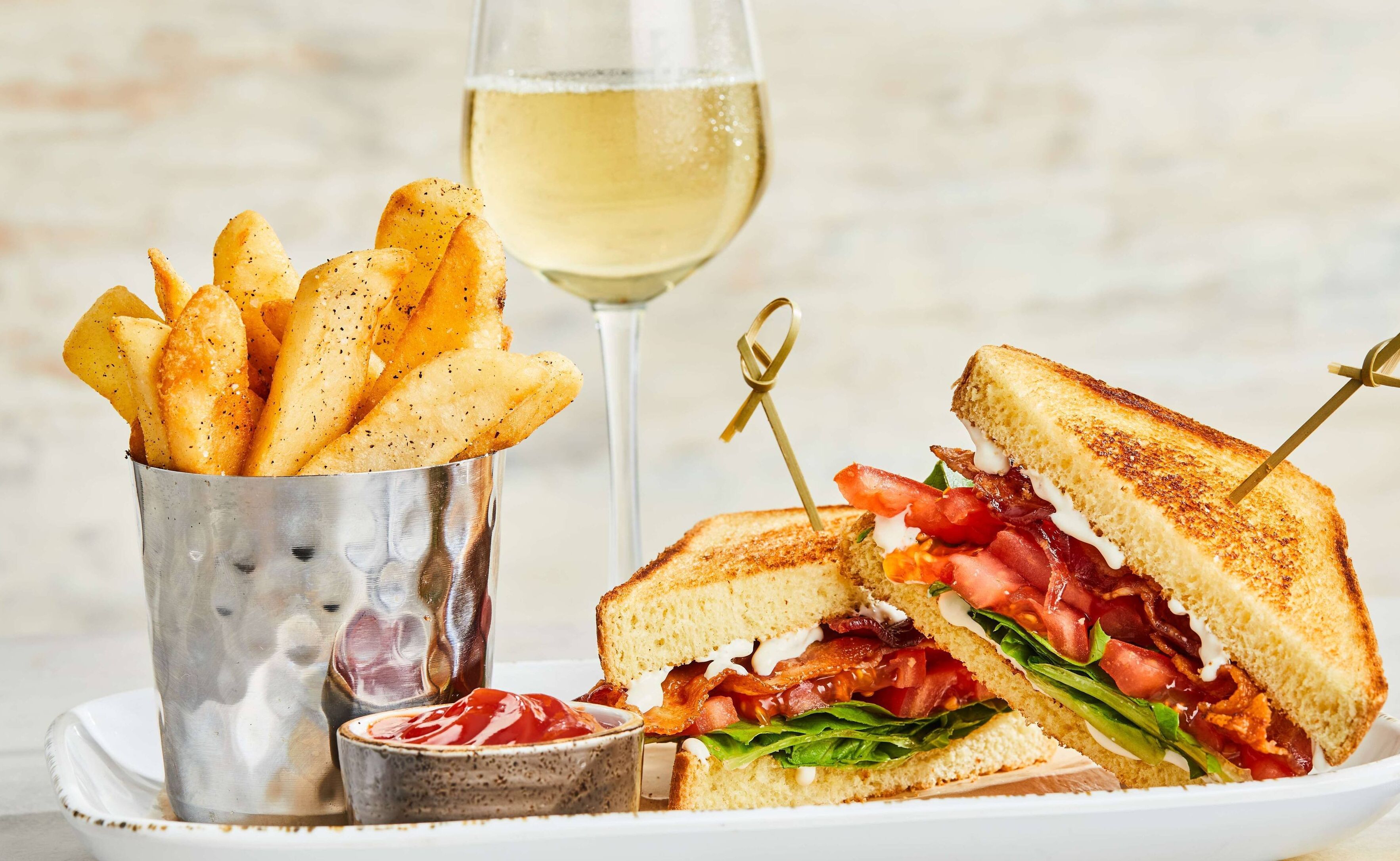 Ein Teller mit einem gegrillten Sandwich, Pommes und einem Glas Weißwein.