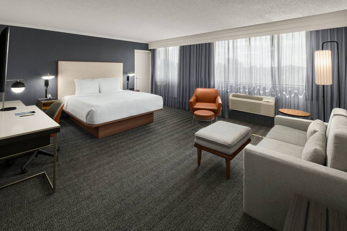 Habitación de hotel con una cama grande, un escritorio, una silla, un sofá y una mesita.