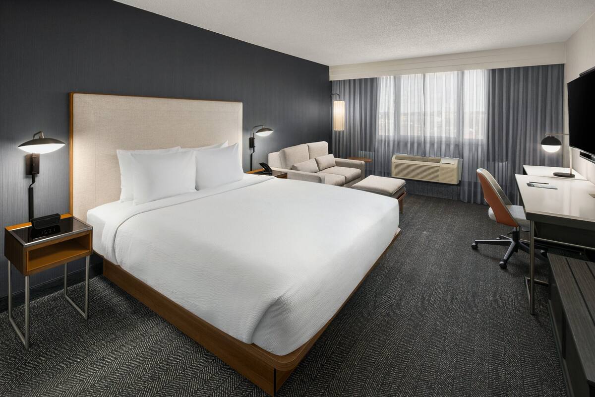 Una habitación de hotel moderna con una cama grande, un escritorio, una silla y un sofá.