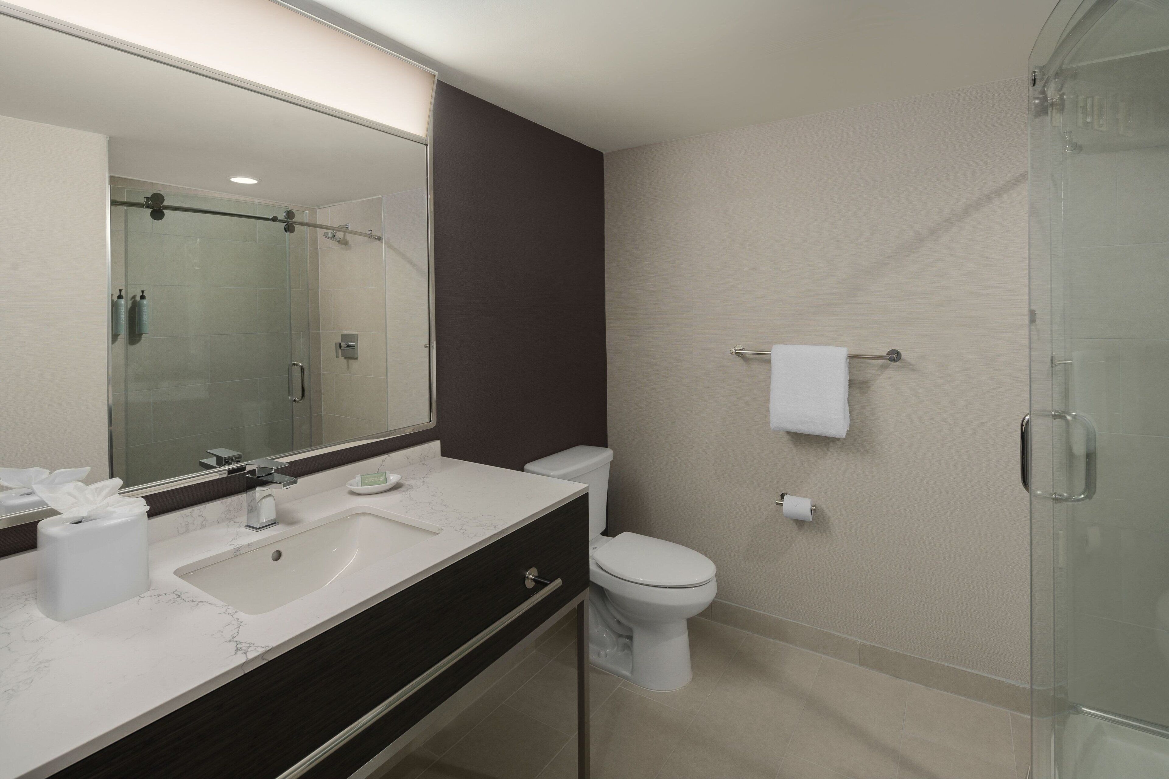 Un baño moderno con un espejo grande, dos lavamanos, un inodoro y una cabina de ducha de vidrio.