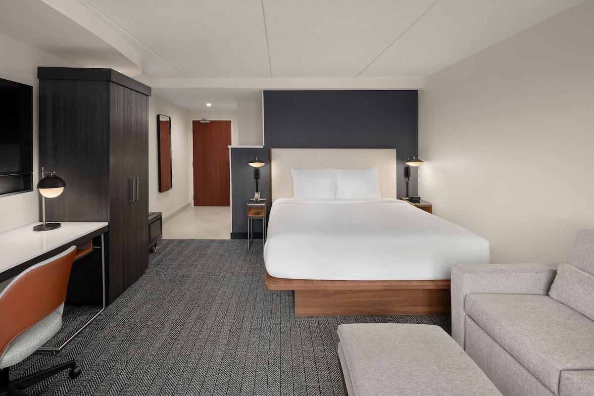 Una habitación de hotel con cama, escritorio, sillón, sofá y televisión.