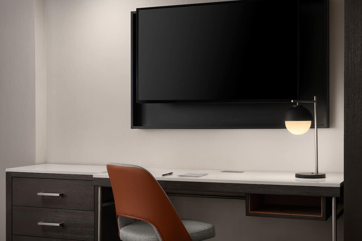 Un escritorio moderno con un monitor de pantalla plana, una lámpara de escritorio y una silla.
