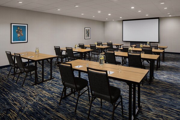 A conference room with multiple tables and chairs, a projector screen, and two framed artworks on the walls. - Courtyard New Haven at Yale (New Haven)