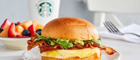 Un sándwich de desayuno en un plato, con una taza de Starbucks al fondo.