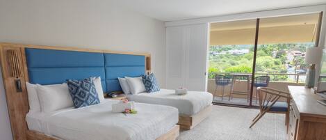 Habitación de hotel con dos camas, un escritorio y un balcón con vistas a la vegetación.