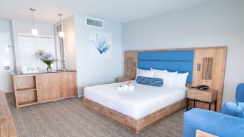 Une chambre d’hôtel moderne avec un cadre de lit en bois, une tête de lit bleue, une table de chevet en bois et un fauteuil bleu.
