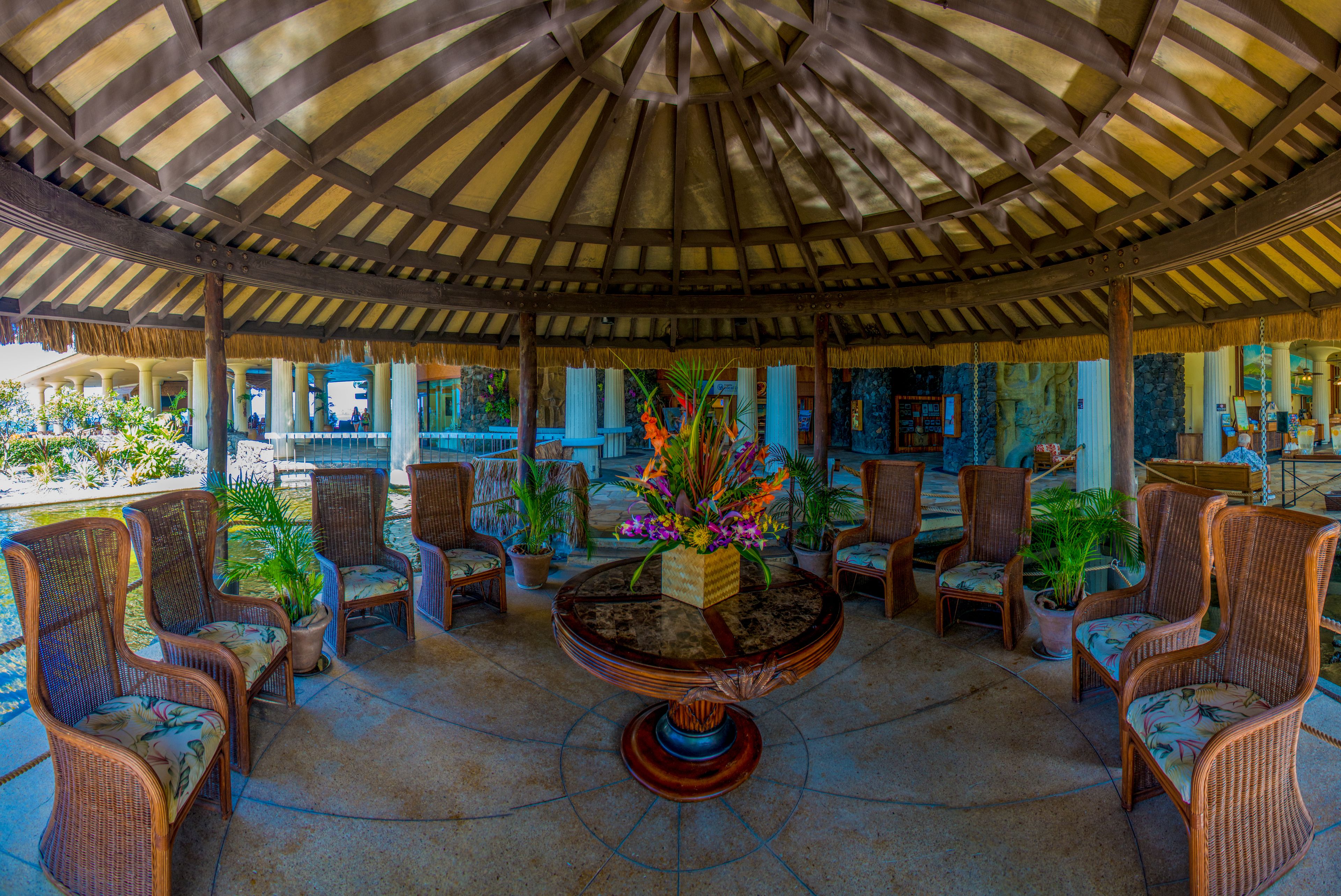 A covered outdoor seating area with wicker chairs and a central table with a floral arrangement.