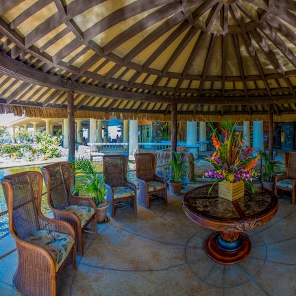 A covered outdoor seating area with wicker chairs and a central table with a floral arrangement.