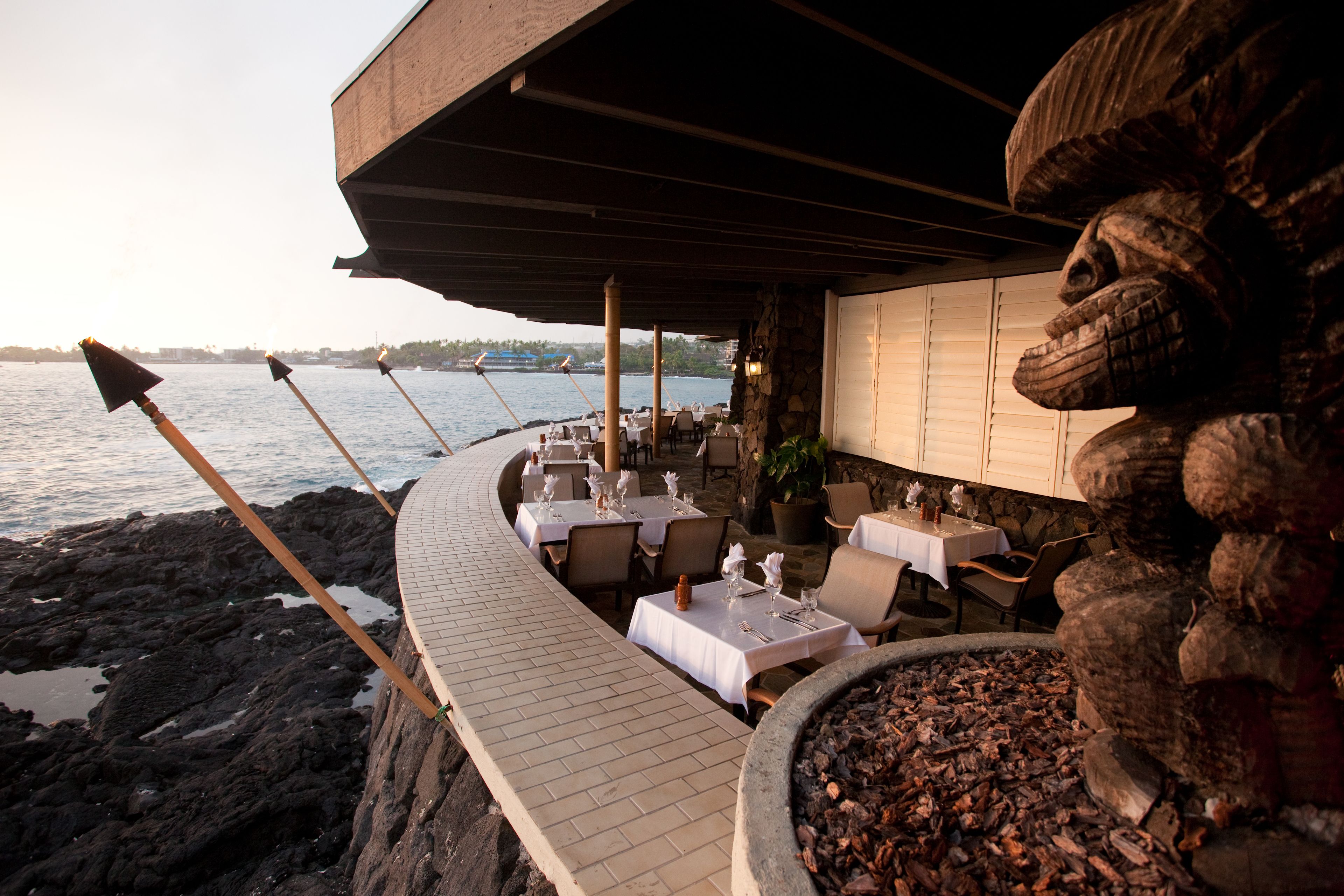 An outdoor dining area with tables and chairs, overlooking a body of water.