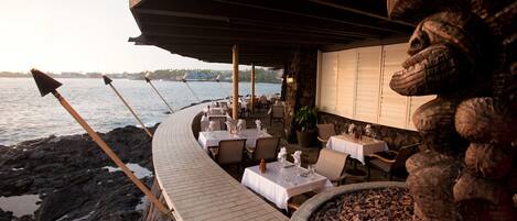 An outdoor dining area with tables and chairs, overlooking a body of water.