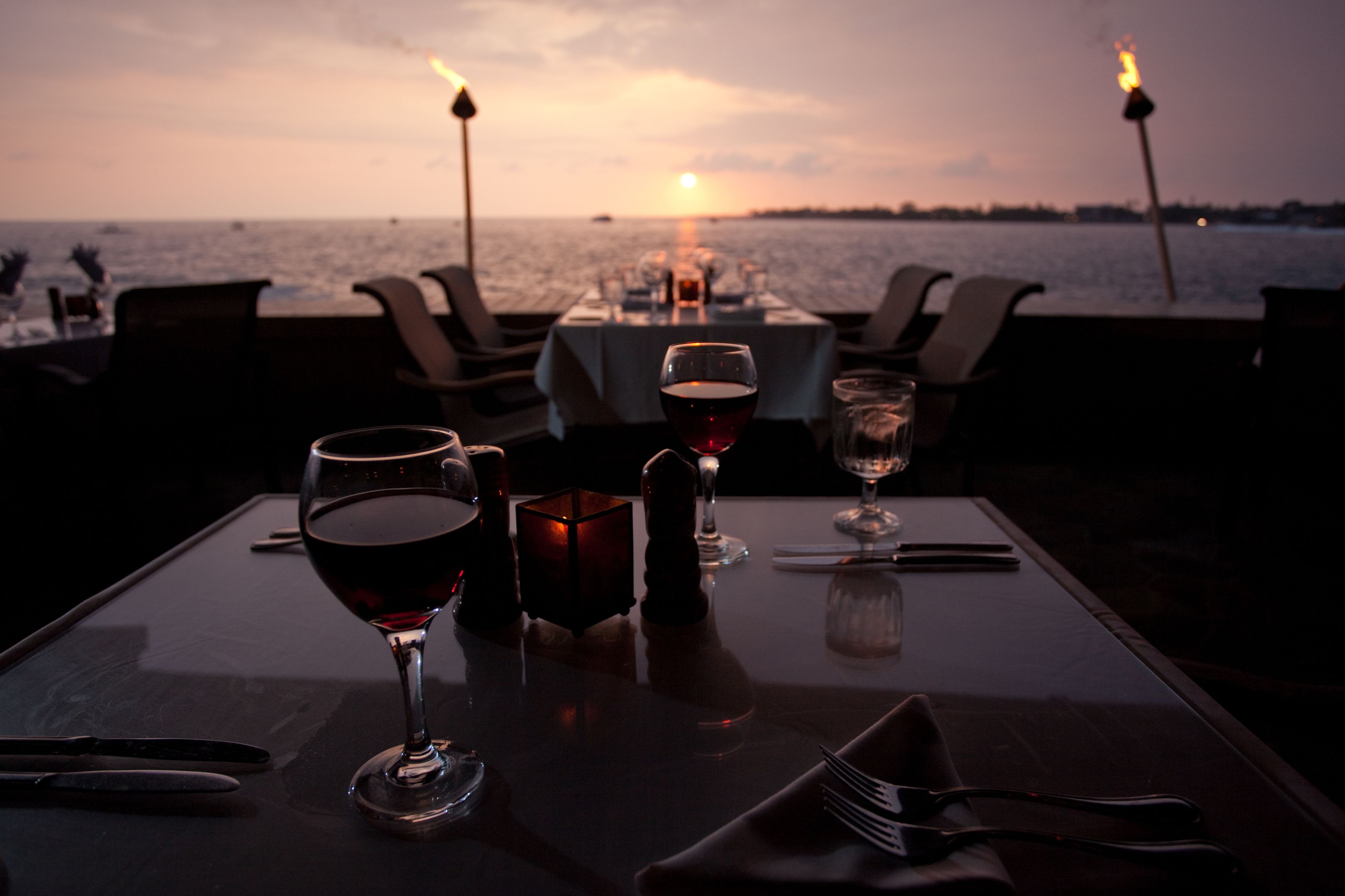Una tavola imbandita per due, con bicchieri da vino e una candela, con vista su un tramonto sull'acqua.