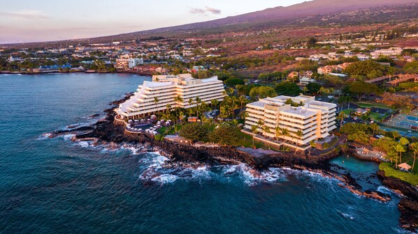 A coastal hotel with multiple buildings, a rocky shoreline, and a view of the surrounding town and hills. - Royal Kona Resort (Kailua-Kona)