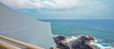 A coastal view with a white sail, rocky shoreline, and calm sea.
