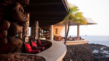 A curved outdoor seating area with red cushions, a stone wall, and a view of the ocean.
