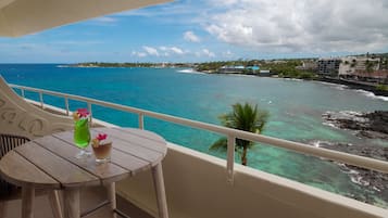 A balcony with a view of the ocean, a table with drinks, and a chair.