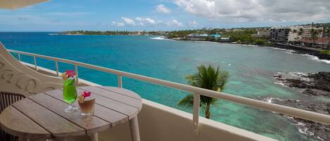 A balcony with a view of the ocean, a table with drinks, and a chair.