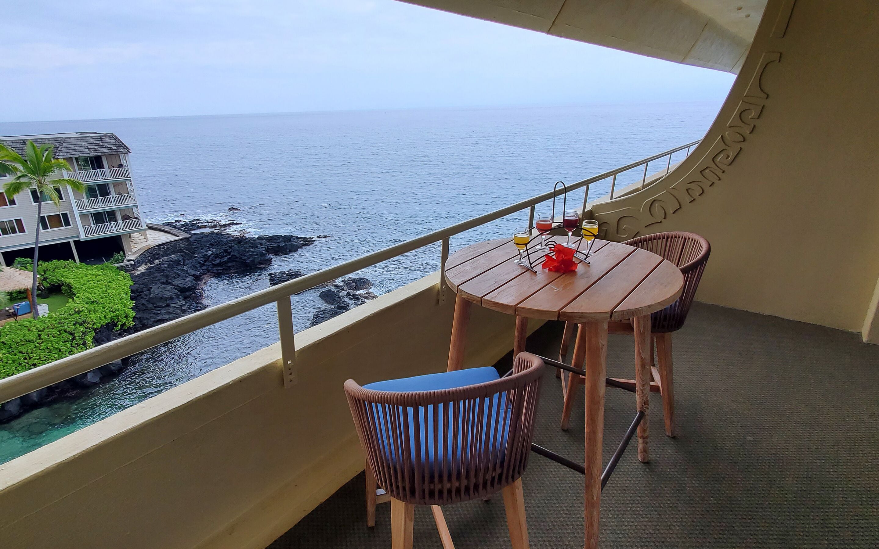 Un balcón con mesa y sillas, con vistas a un litoral rocoso y el océano.