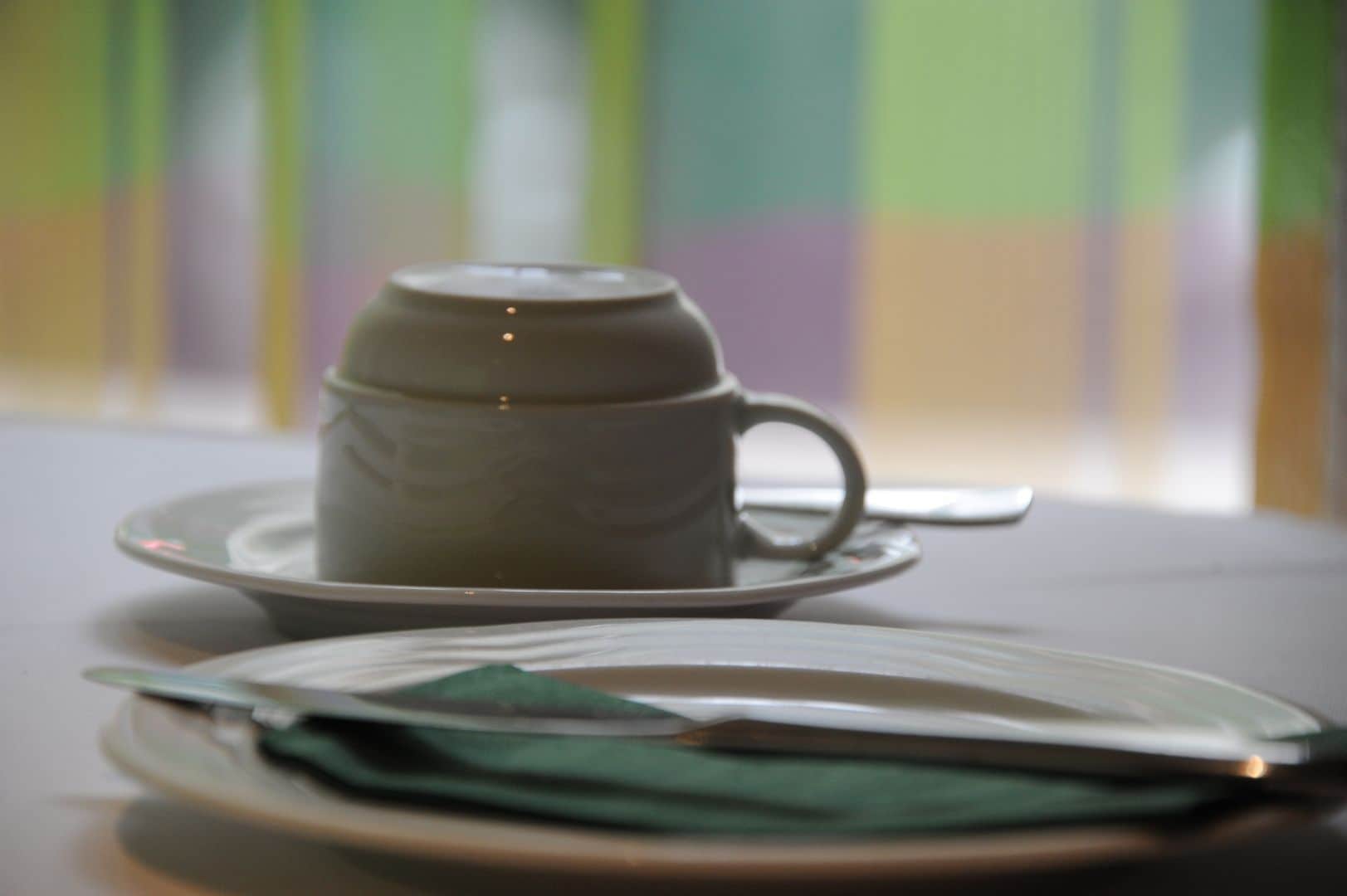 A cup and saucer on a table with a napkin and a spoon.