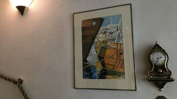 Un cuadro enmarco con un barco en la pared, un reloj sujeto a la pared y una lámpara.