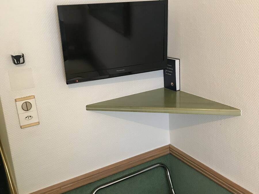 A television mounted on a wall, a power outlet, and a metal chair.
