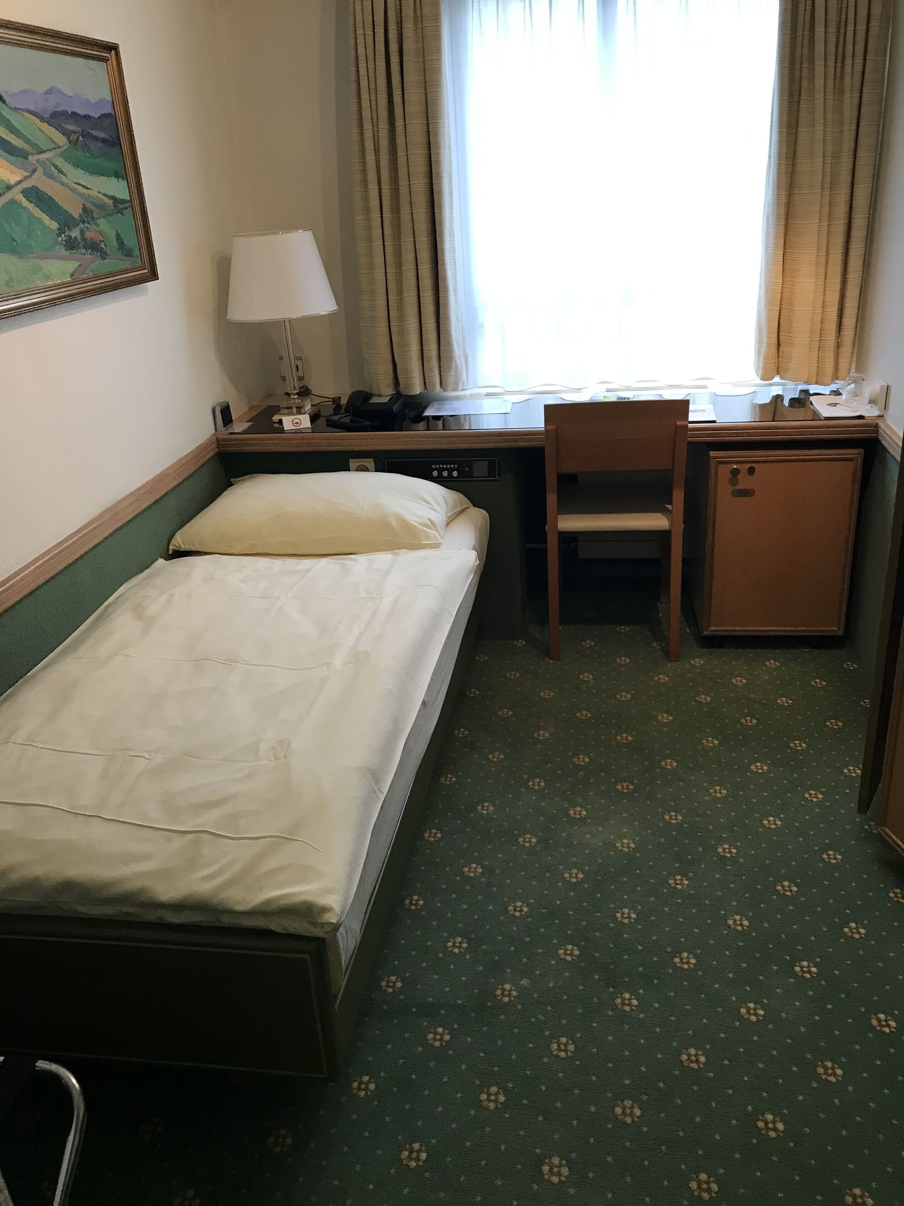 Quarto de hotel com cama, escrivaninha, cadeira e um pequeno armário.