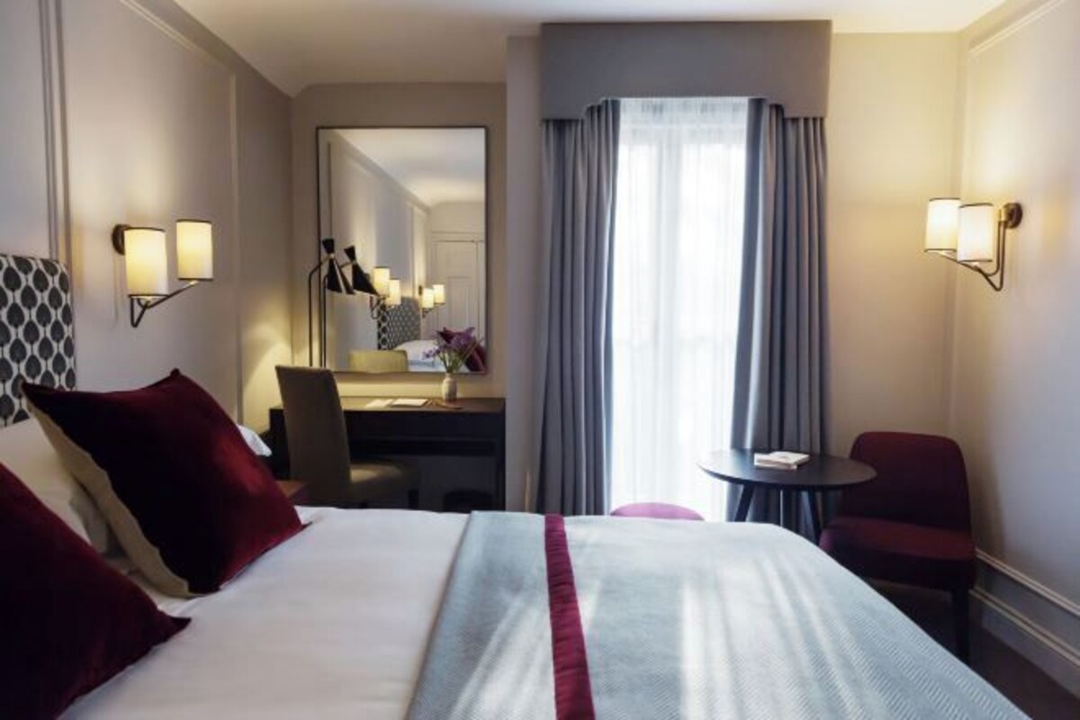 A hotel room with a large bed, a desk, a chair, and a small table.
