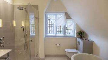 Un baño con ducha envuelta en vidrio, inodoro, bañera y ventana con cortinas.