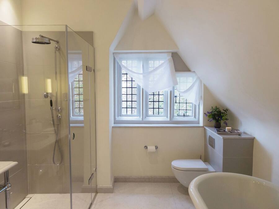 A bathroom with a glass-enclosed shower, a toilet, a bathtub, and a window with curtains.