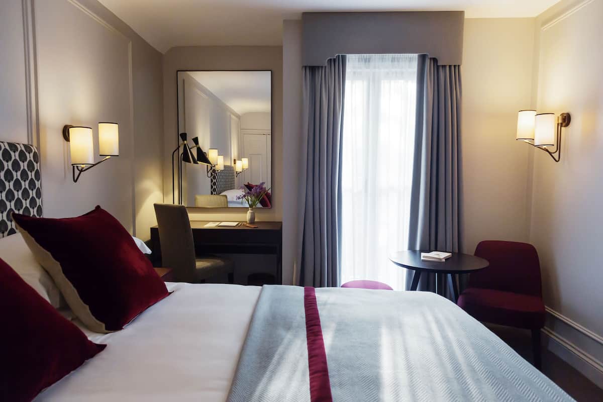 A hotel room with a large bed, a desk, a chair, and a small table.