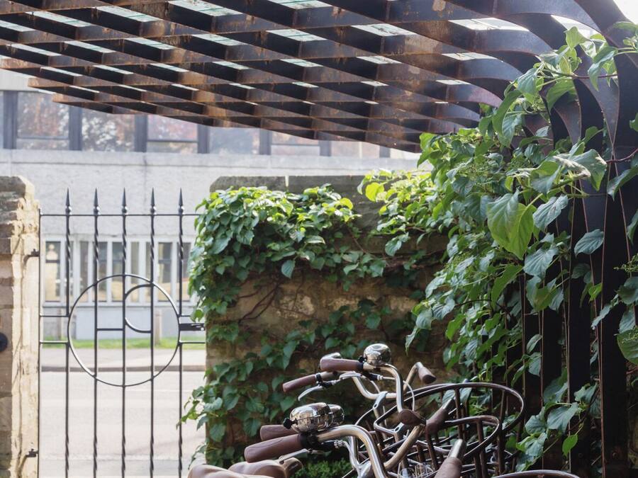 Un área de estacionamiento para bicicletas techada, con valla metálica y vegetación.