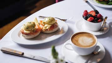 Une table dressée pour le petit-déjeuner avec des œufs Bénédicte, un bol de fruits rouges variés et une tasse de café.