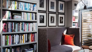 Una habitación con una estantería llena de libros, un sofá gris con un cojín rojo y una mesa redonda con un libro.