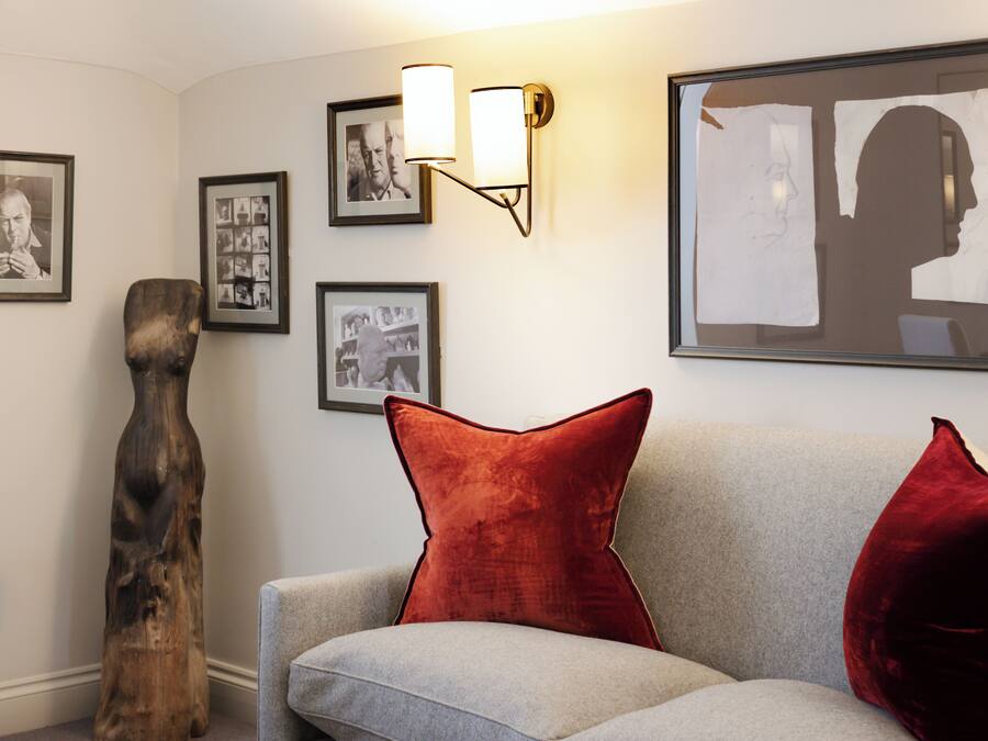 A living room with a grey sofa, red cushions, a wooden sculpture, and framed photographs on the wall.