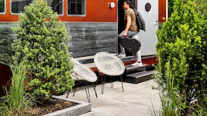 A train with a person exiting, surrounded by greenery and outdoor seating.