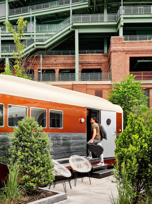 A train with a person exiting, surrounded by greenery and outdoor seating.