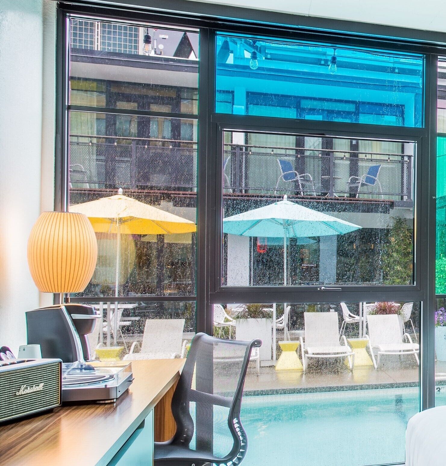 Ein Zimmer mit Blick auf einen Pool, ein Schreibtisch mit Computer und einem alten Radio, und zwei Sonnenschirme draußen.