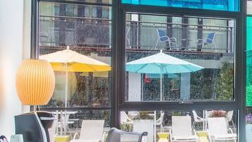 Ein Zimmer mit Blick auf einen Pool, ein Schreibtisch mit Computer und einem alten Radio, und zwei Sonnenschirme draußen.