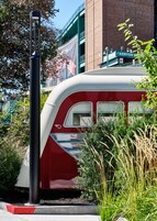 A stationary train with a red and white color scheme, surrounded by greenery and a building with a sign that reads "KENYON".