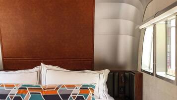 A bed with white linens, a colorful geometric pillow, and an orange throw blanket.